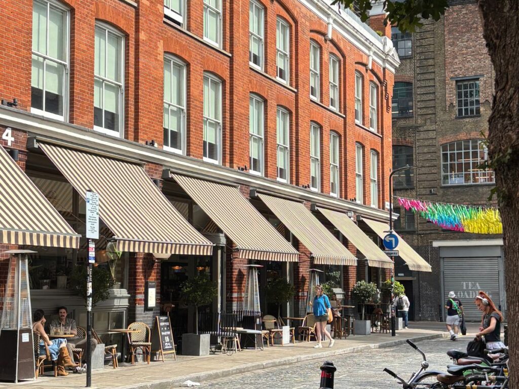 Exterior of a red brick building with Georgian-style windows and awnings covering outdoor cafe seating outside the Boundary Hotel in Shoreditch, London