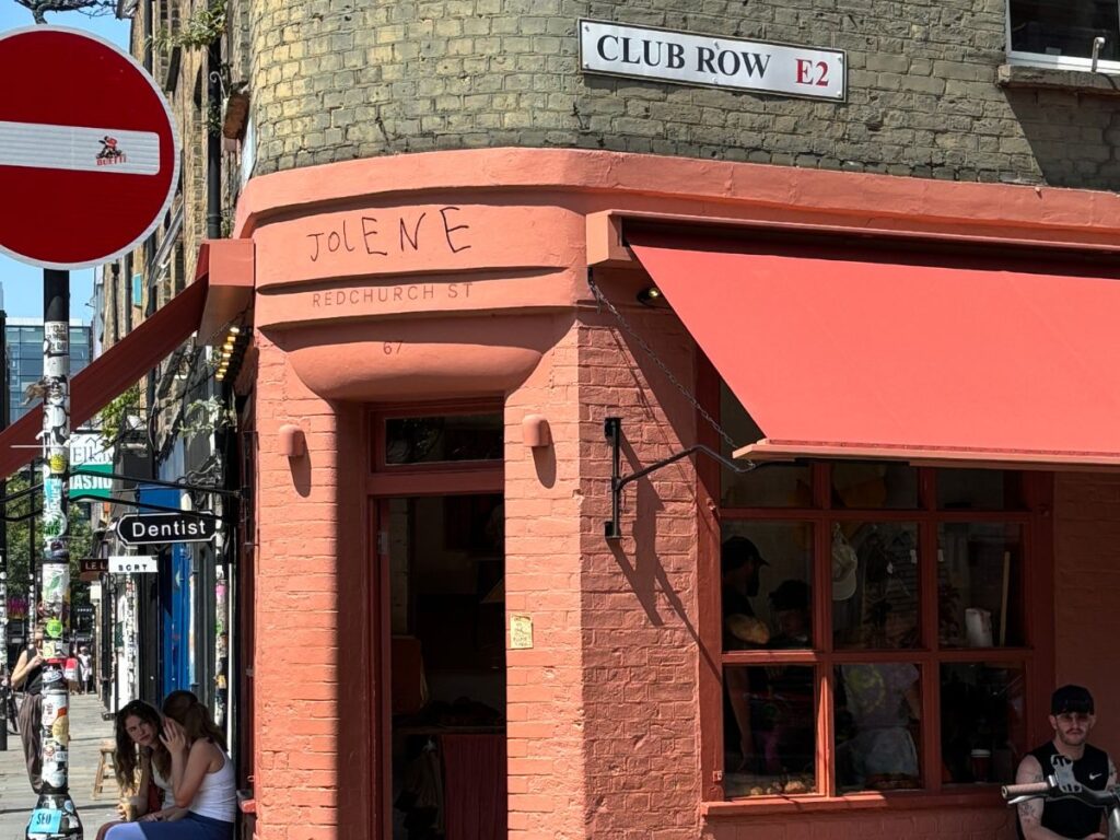 Brightly colored exterior of Jolene Bakery on the corner of Club Row in Shoreditch. Terracotta panted brick wall with similar color awning and window frames.