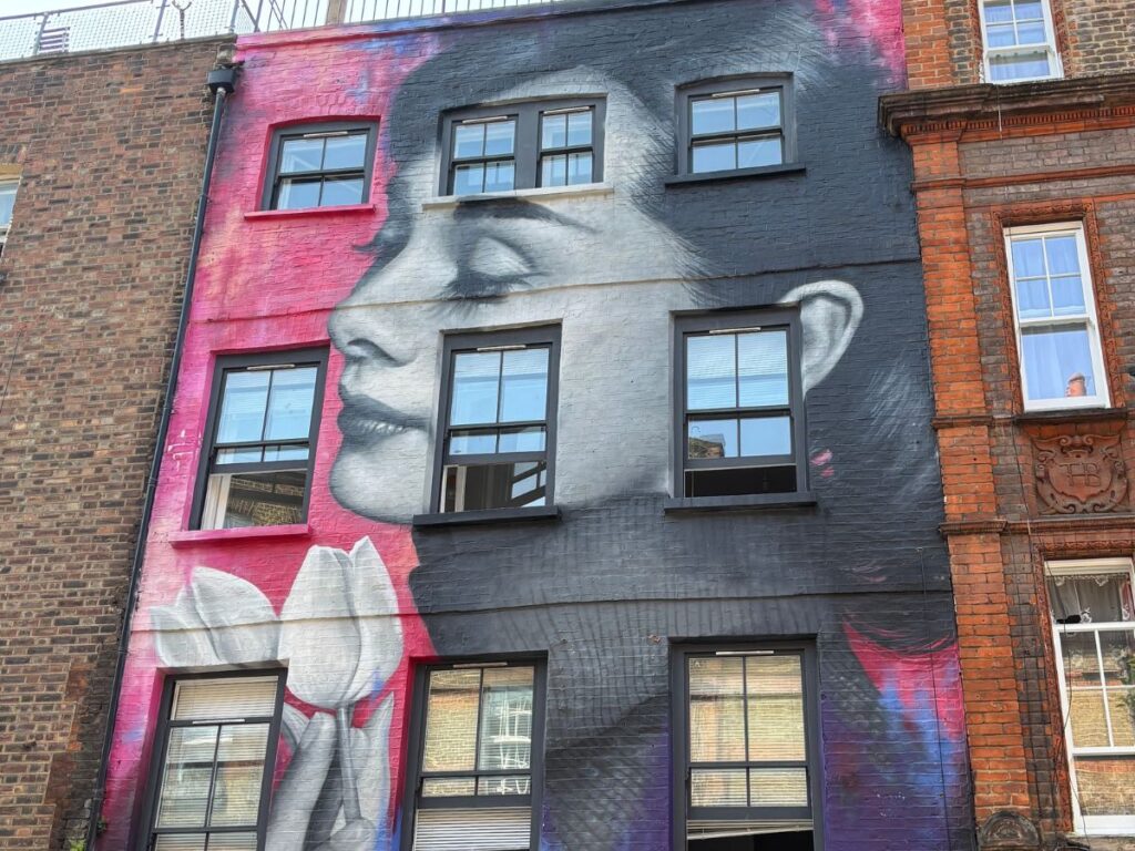 Example of street art on Brick Lane in Shoreditch, London that depicts a portrait of Audrey Hepburn pained onto a brick building in pinks and blues.