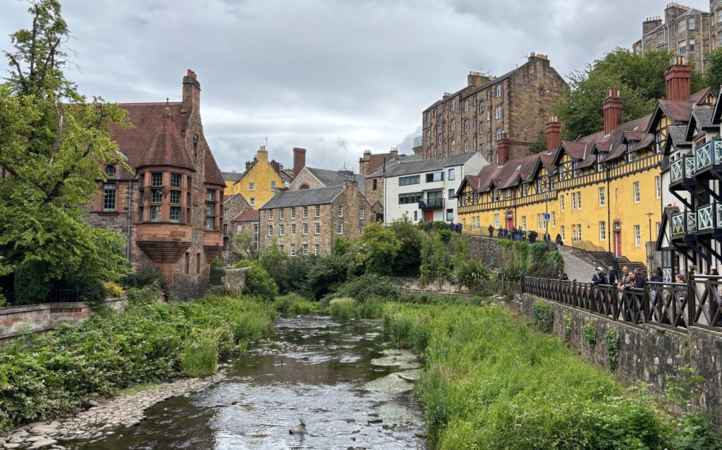 Dean Village in Edinburgh with the Water of Leith flowing toward Stockbridge, lined by historic stone buildings and greenery.