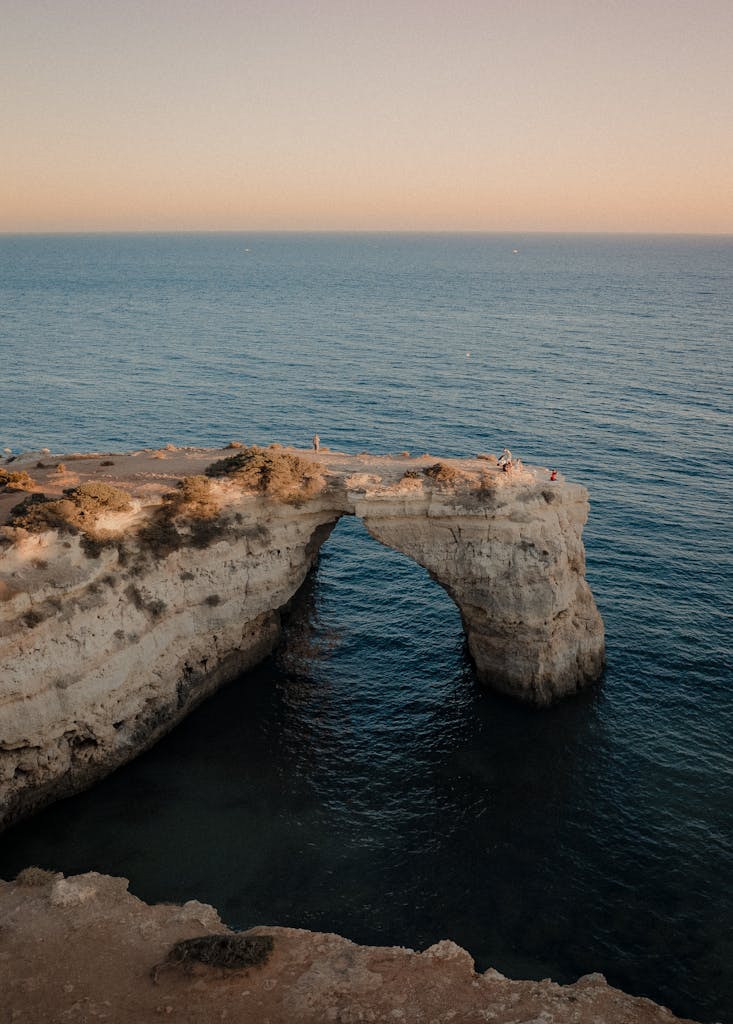 A breathtaking aerial view of the Arco de Albandeira rock formation in Algarve, Portugal during sunset.