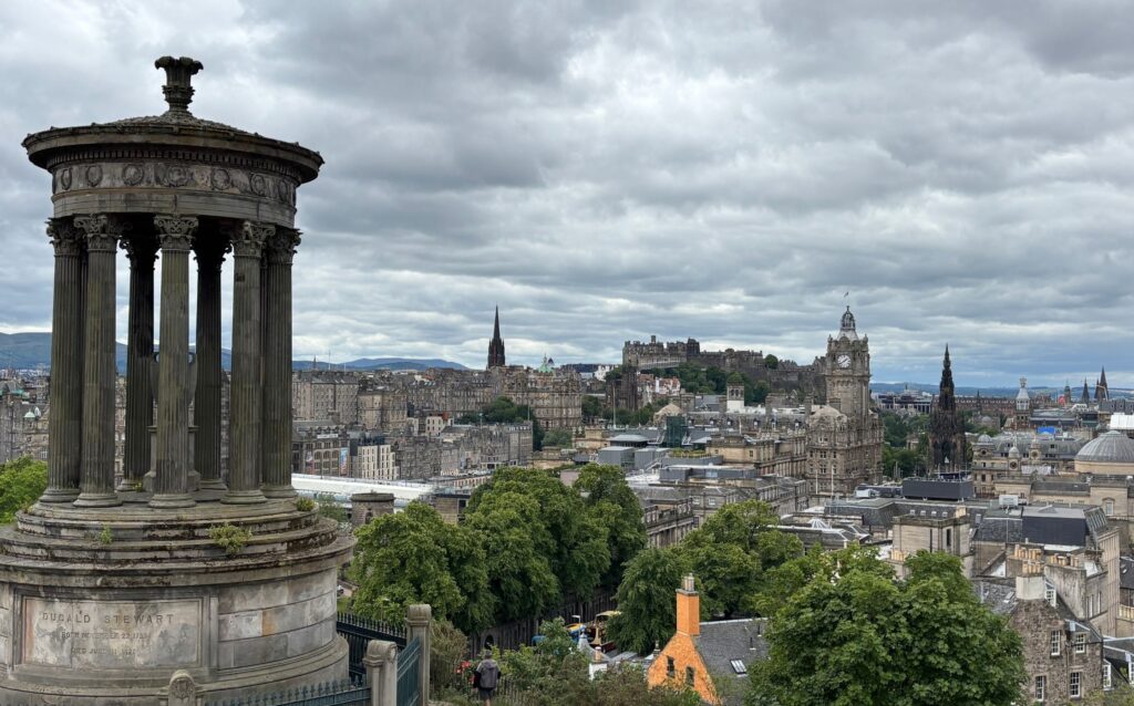 Calton Hill in Edinburgh looking toward Edinburgh Castle with the Dugald Stewart Monument in the foreground under cloudy skies.
