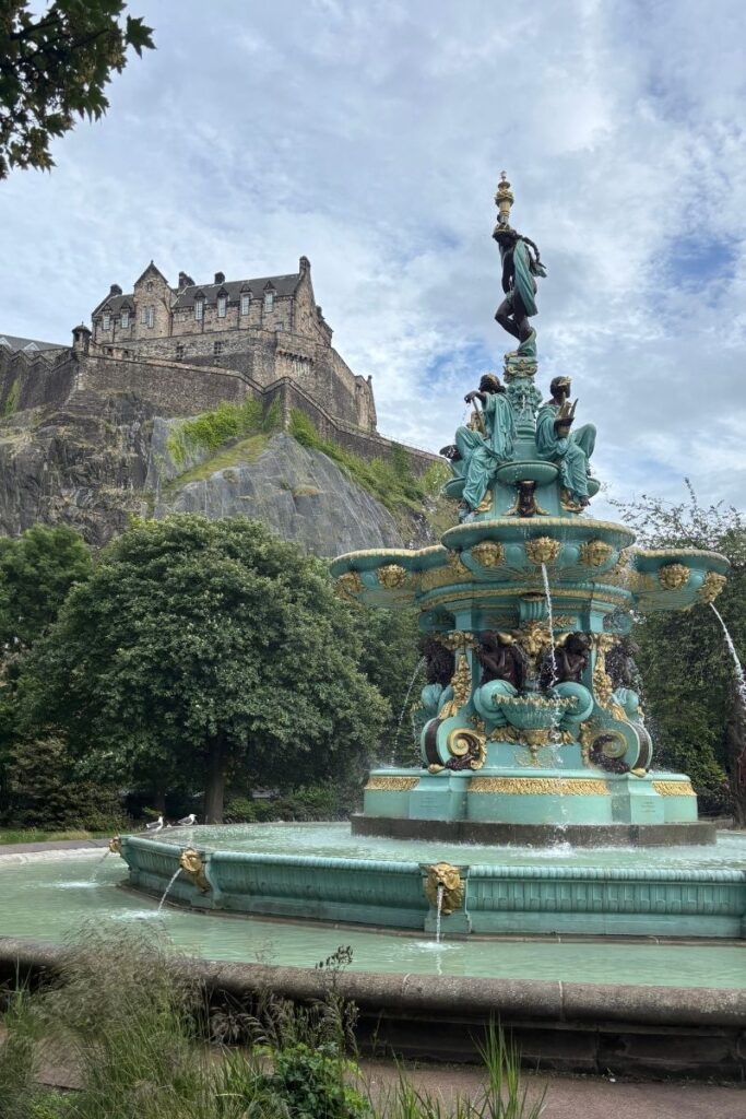 Ross Fountain in Princes Street Gardens, Edinburgh, with Edinburgh Castle rising in the background under cloudy sky.