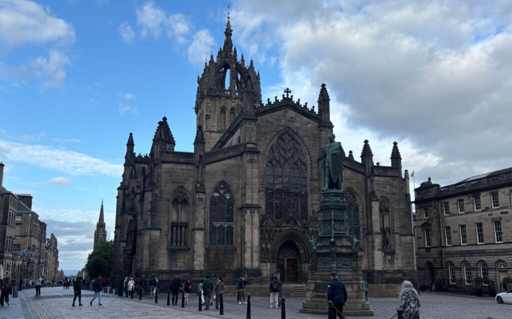 St Giles’ Cathedral on the Royal Mile in Edinburgh, with the bronze statue of Adam Smith in front on entrance and Gothic Old Town architecture leading down toward the Palace of Holyroodhouse.