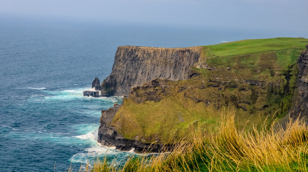 Stunning view of the Cliffs of Moher with grassy tops and blue ocean waves in Ireland.