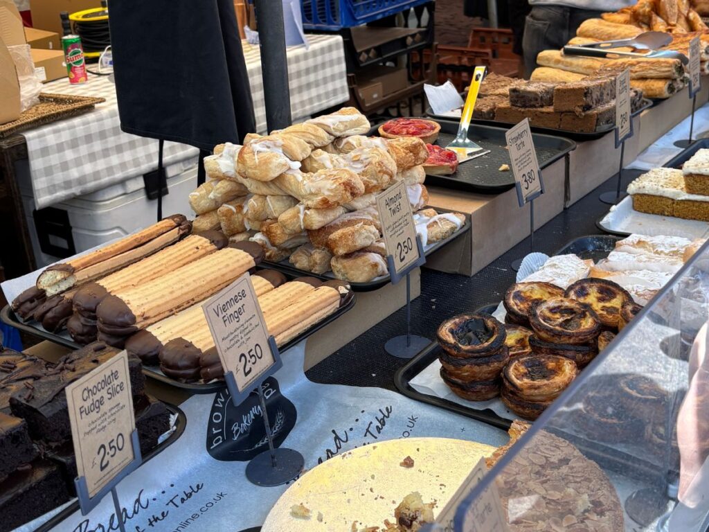 Market stall in Cambridge, England, displaying a variety of baked goods and sweet treats.