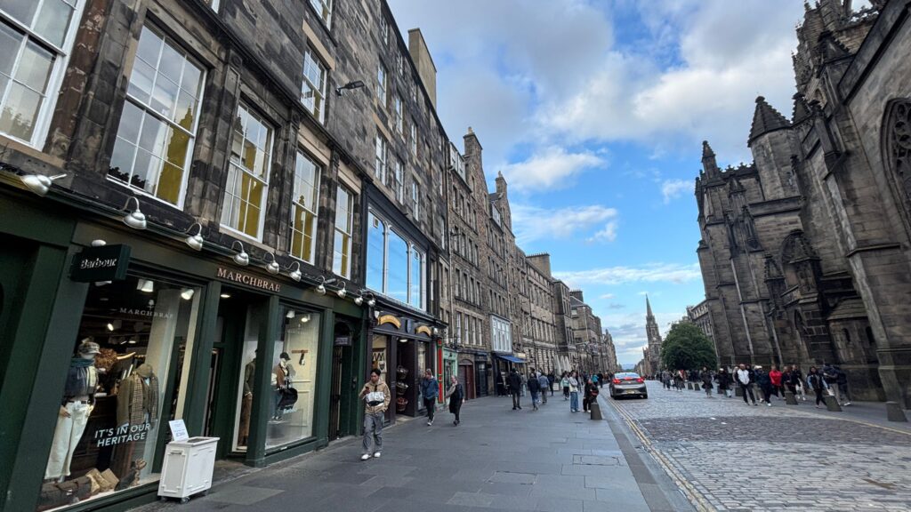 Streetscape of the Royal Mile in Old Town Edinburgh with historic stone buildings, cobblestones, and pedestrians.