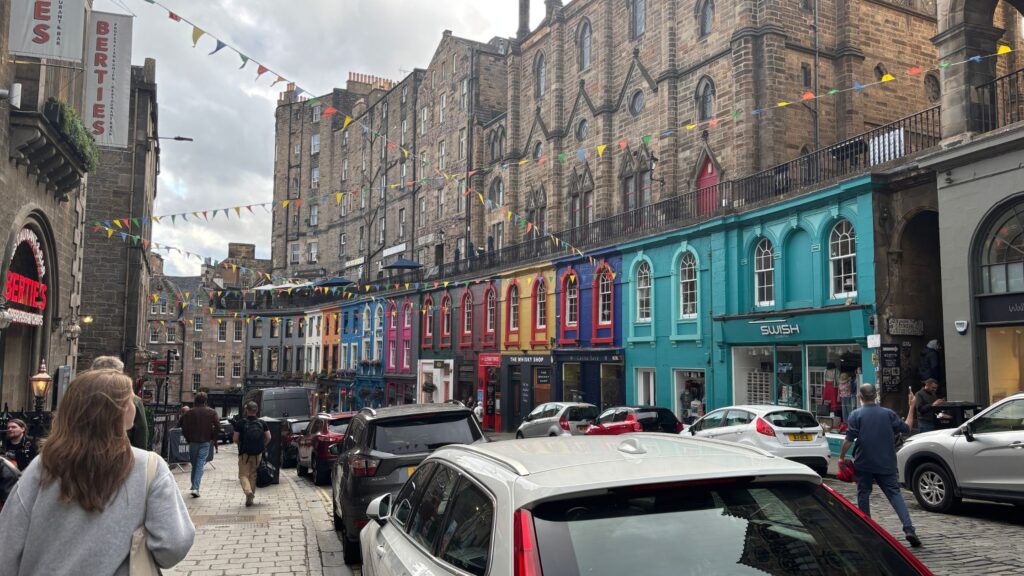 View down Victoria Street in Old Town Edinburgh toward Grassmarket, showing colorful historic buildings and pedestrians.