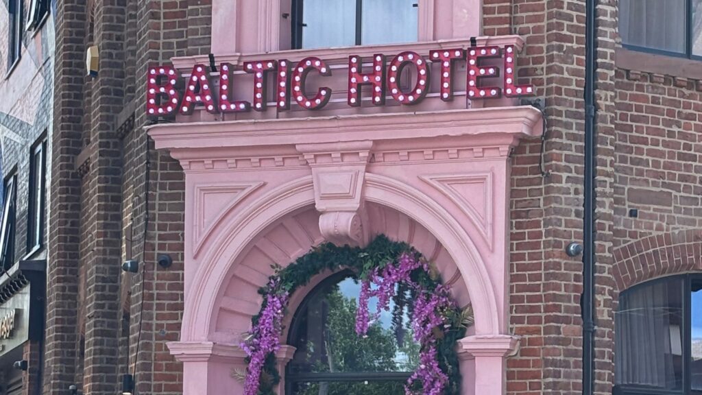 Pink front of Baltic Hotel in Liverpool's Baltic Triangle with neon signage above the door.