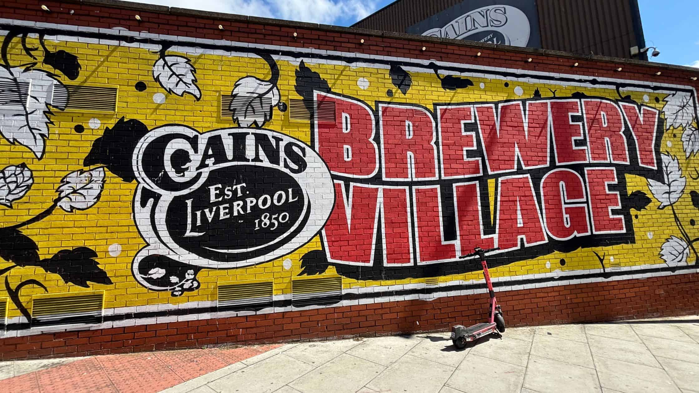 Colorful mural of Cains Brewery Village in Liverpool's Baltic Triangle with red lettering and yellow background.