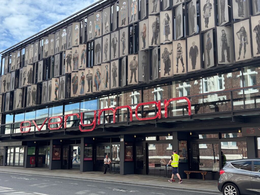Front exterior of the Everyman Theatre on Hope Street Liverpool, featuring the iconic red Everyman lettering and a striking facade made up of over a hundred life-sized portrait shutters representing ordinary Liverpool residents