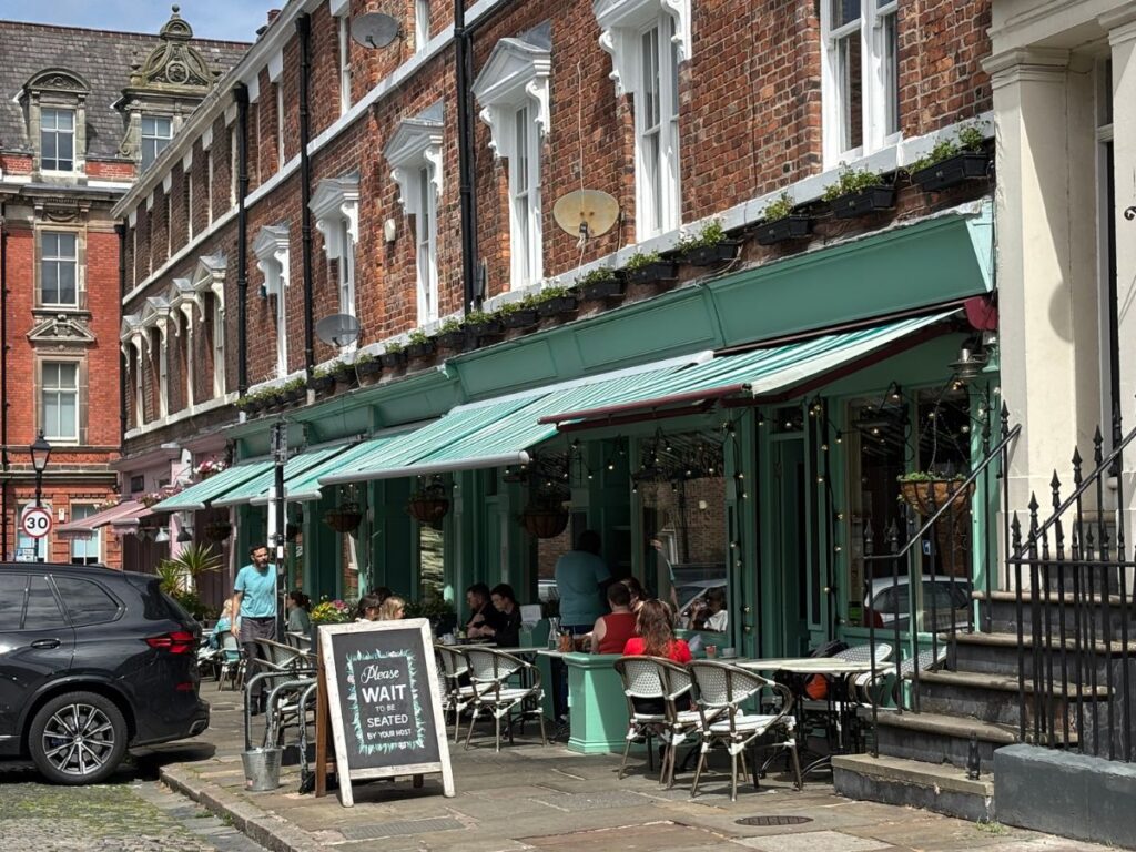 Green awning of The Quarter cafe and outdoor seating restaurant on historic Falkner Street which features classic Georgian architectural homes and cobblestone street.