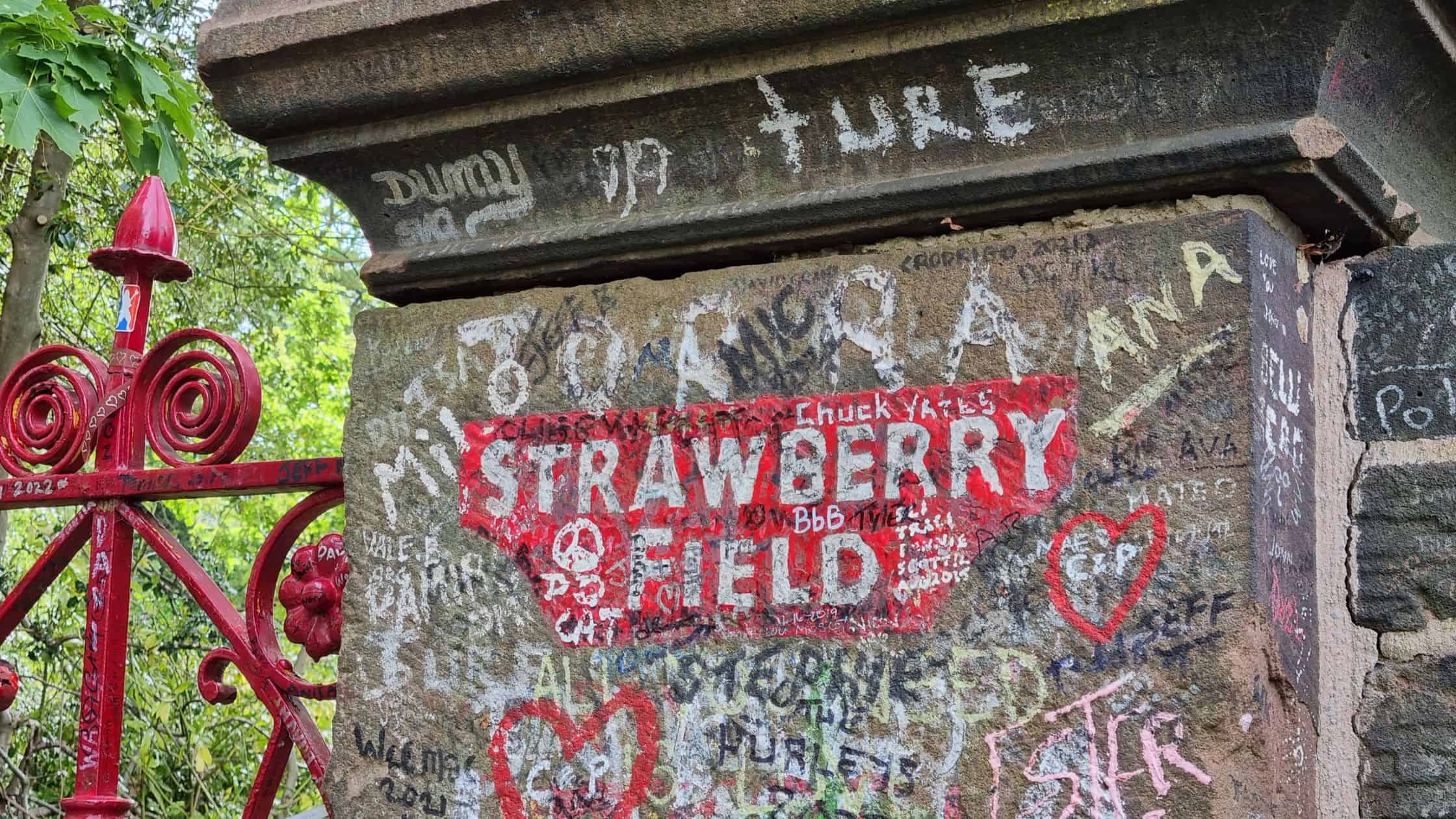 Famous Strawberry Field sign in red and white lettering with graffiti.
