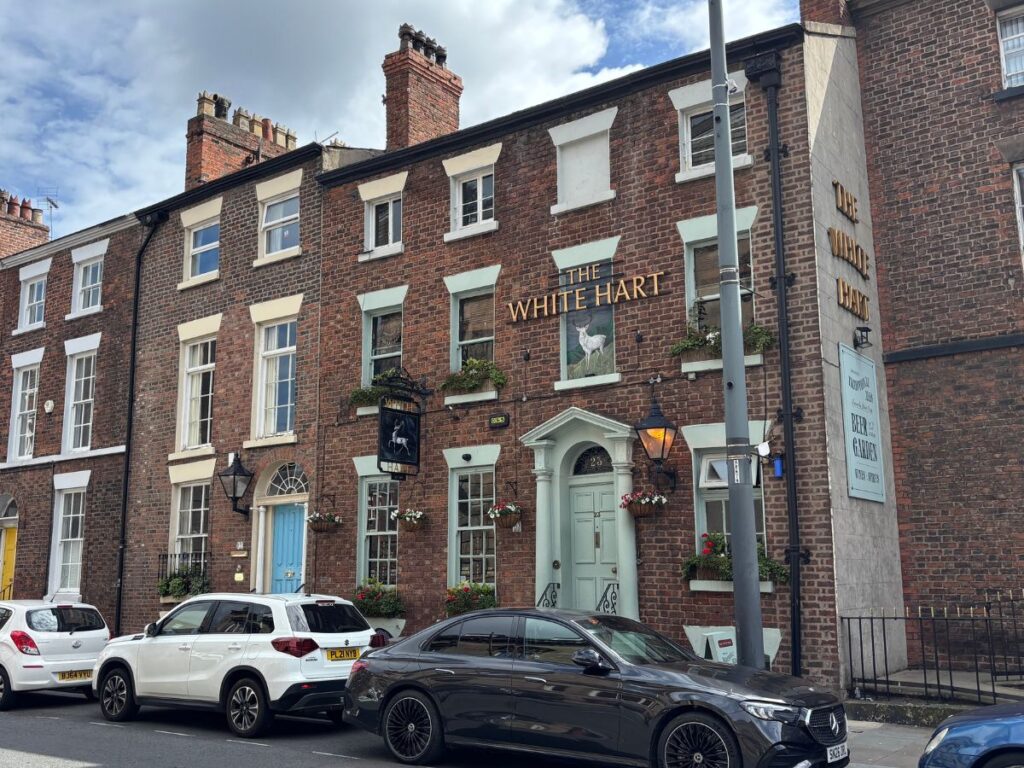Facade of White Hart Pub on Liverpool's Hope Street ih red brick Georgian Terrace building with cars parked along the street out front.