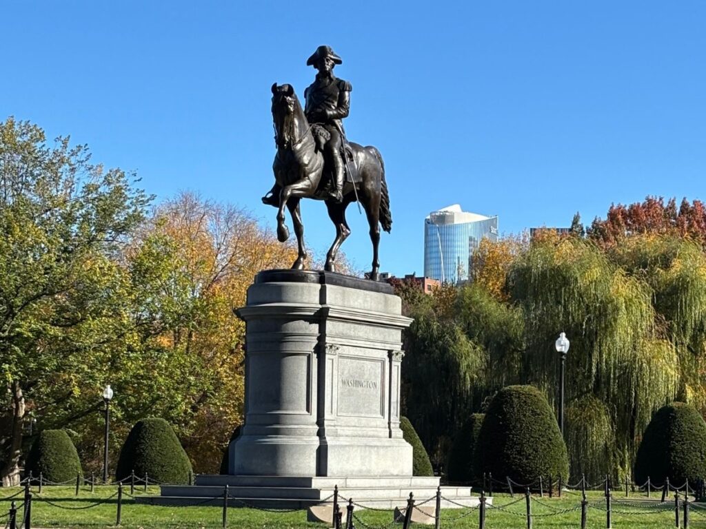 George Washington statue in Boston Public Garden with fall-colored trees and bright autumn sunlight.