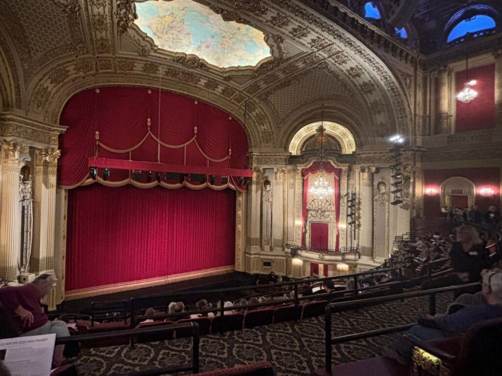 Interior of Citizens Bank Opera House in Boston with lush red curtains, ornate balconies, and decorative plasterwork.