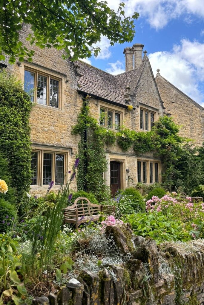 Traditional honey-stone Cotswolds cottage surrounded by vibrant flowers and an English country garden.