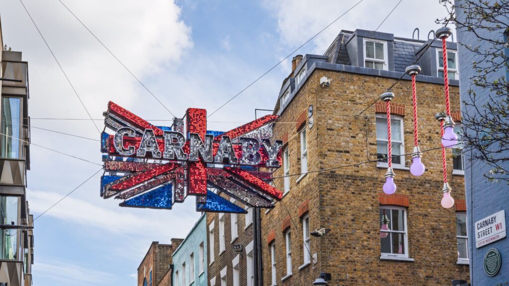Glittering union jack flag suspended over famous Carnaby Street in London in front of brick building.