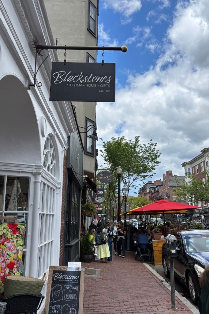 Street scene of Charles St in Boston's Beacon Hill neighborhood with brick sidewalks and store signs.