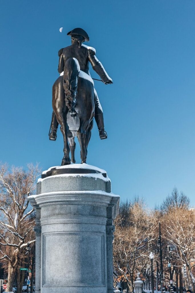 Paul Revere statue as seen from behind in Boston’s North End with winter backdrop, light snow and leafless trees.