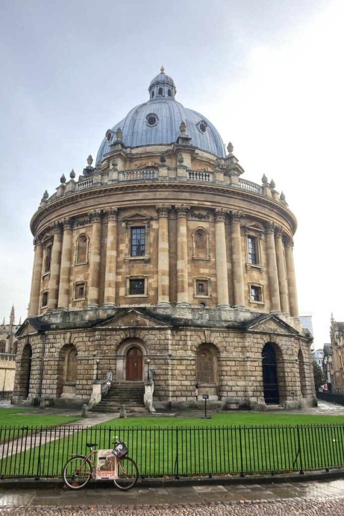 View of the Radcliffe Camera in Oxford with a bicycle resting against metal railings in the foreground.
