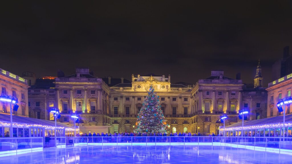 Night time view of ice rink illuminated with blue for Christmas in front of Somerset House in London.