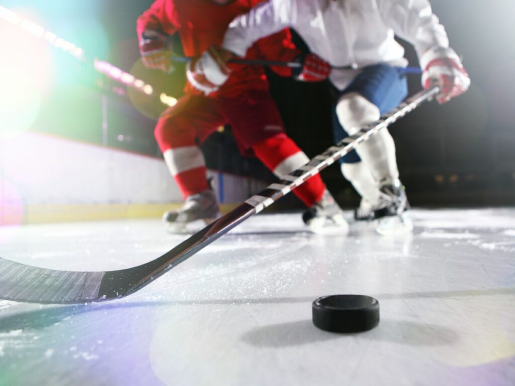 Two ice hockey players on an ice rink competing for the puck with their sticks.
