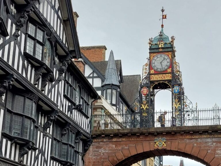 Ornate Eastgate Clock in Chester, England with black and white timber-framed buildings on the right.