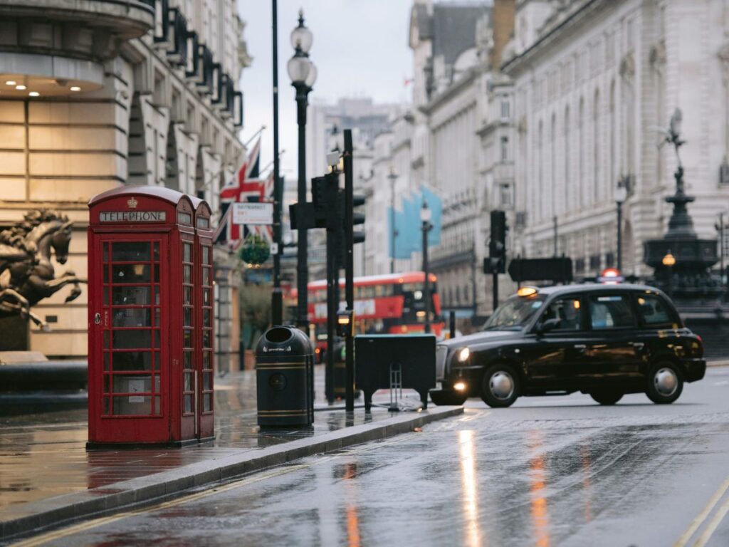 Classic scene of London in rain with wet pavement, red telephone box and black taxi cab on street.