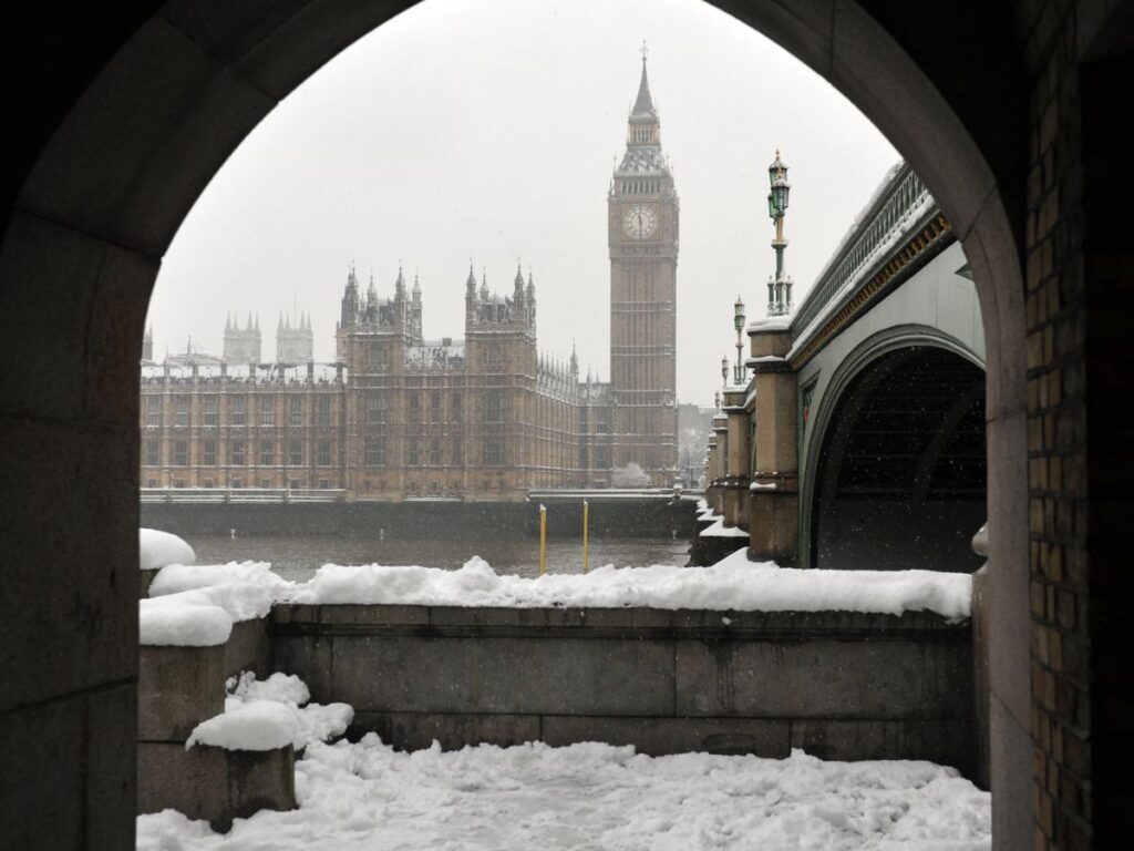 London's Big Ben and Houses of Parliament as seen through arch from south bank of Thames in a snowy winter in London setting.