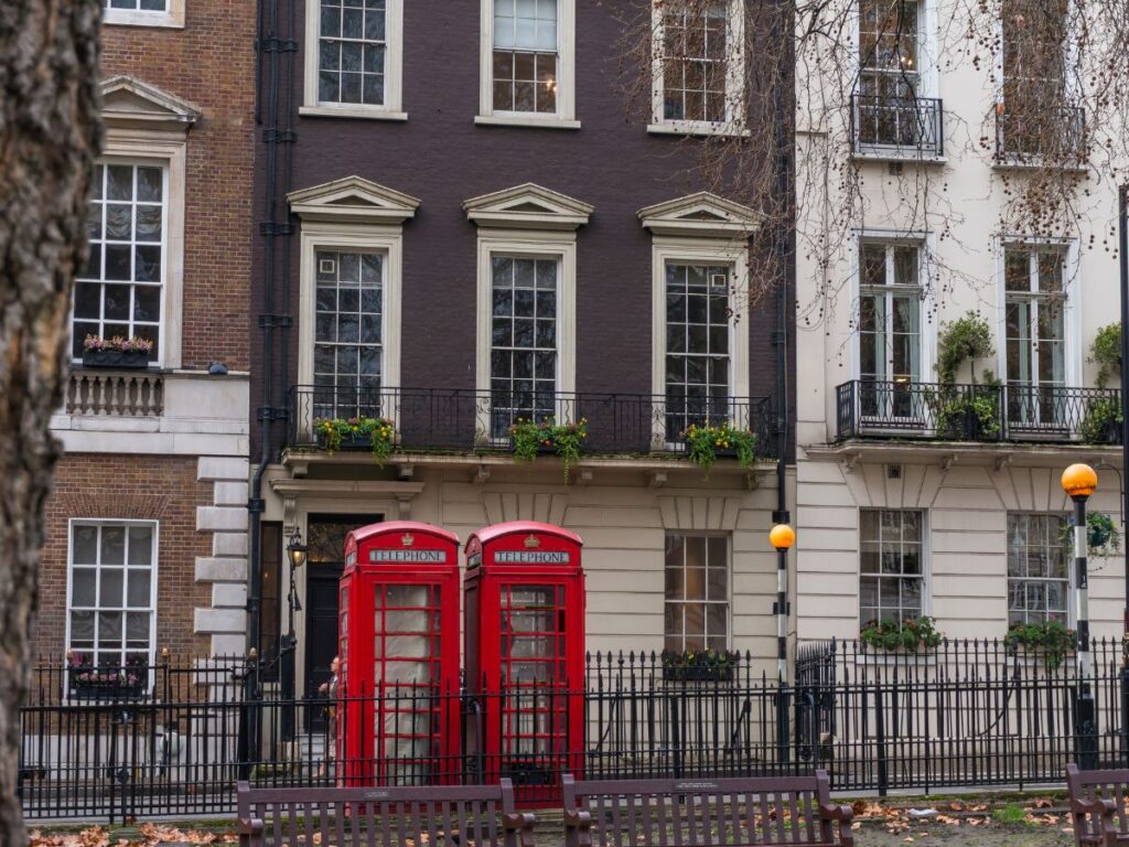 Two red British telephone boxes in front of Georgian style buildings in London's Mayfair neighborhood.