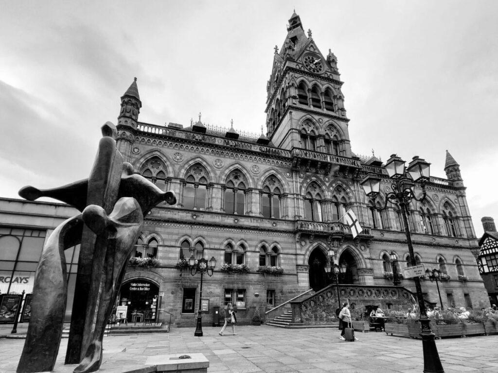 Black and white photo of Chester Town Hall with its central Gothic tower and the Celebration of Chester statue in front.