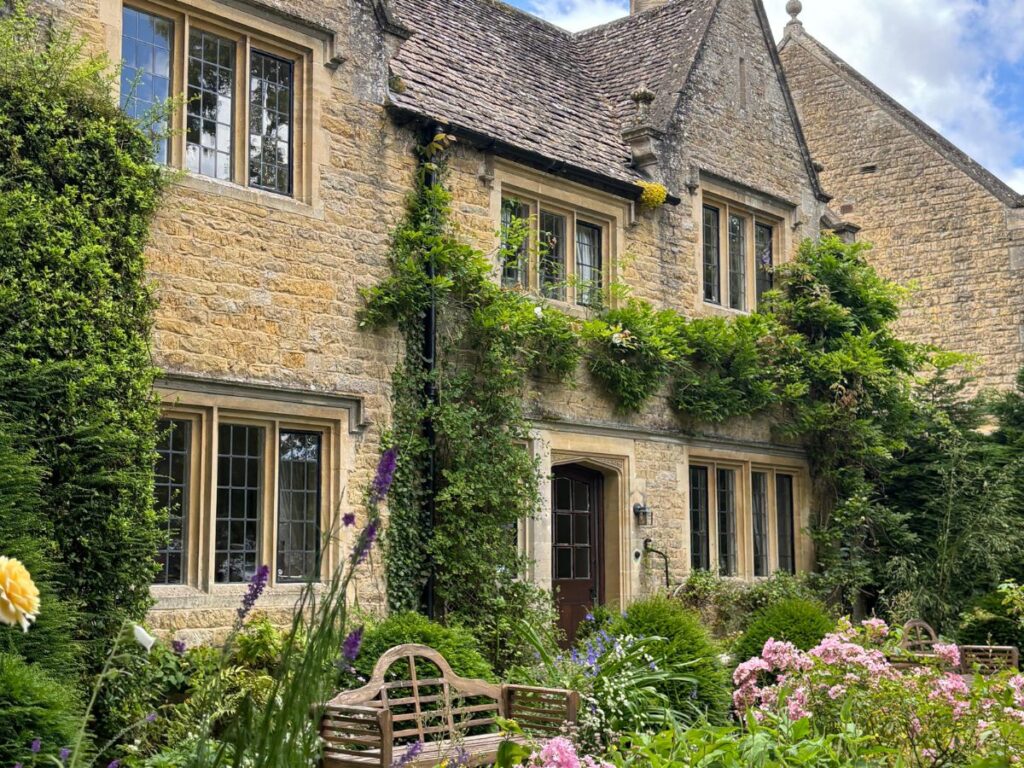 Honey-hued stone cottage in the Cotswolds with English cottage garden at front.