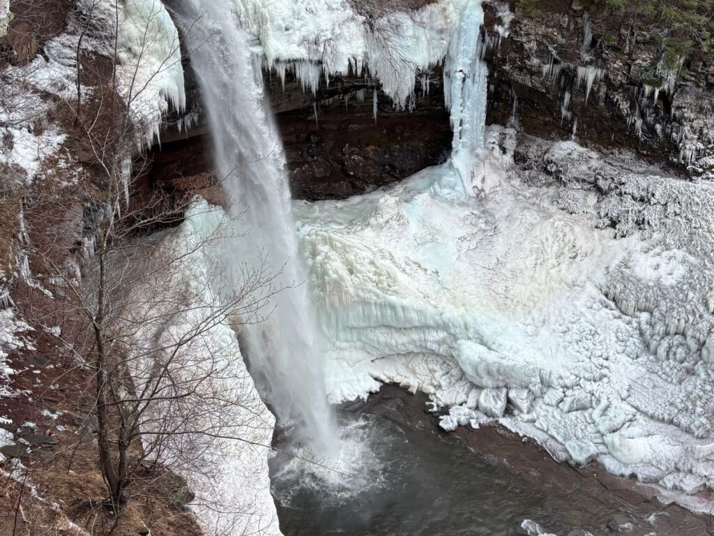 Sheets of ice clinging to Kaaterskill Falls with water tumbling over the ridge in early spring, Catskill Mountains, NY