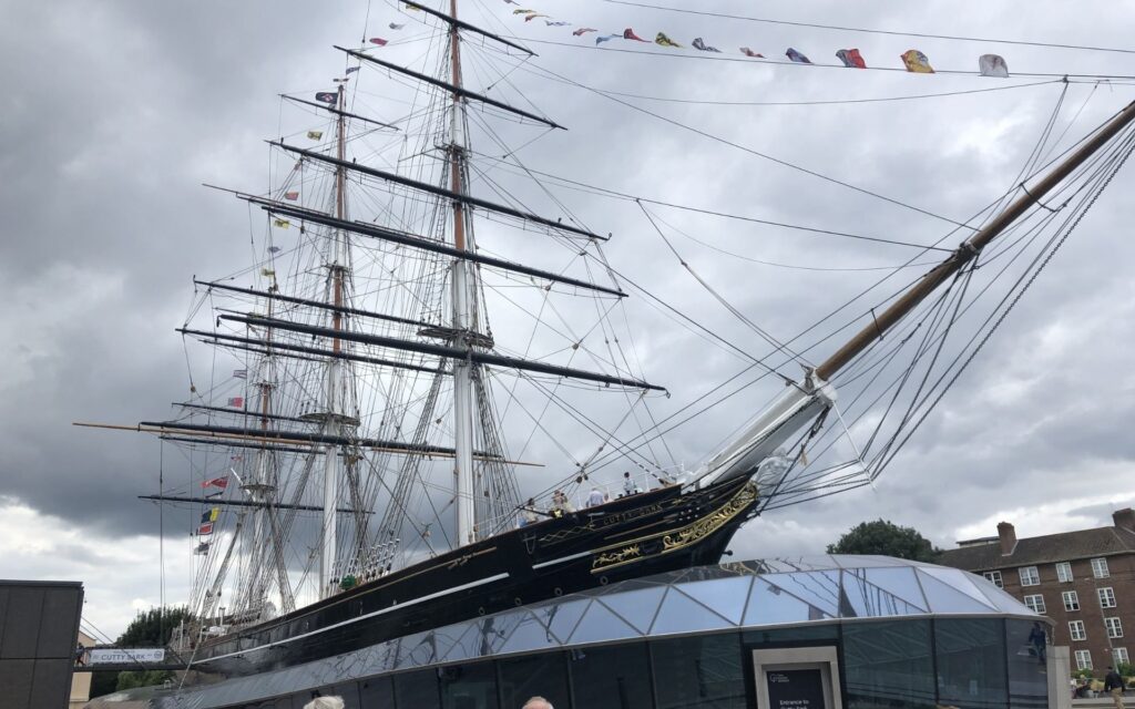 Cutty Sark ship at Greenwich Pier against cloudy sky with flags and rigging.