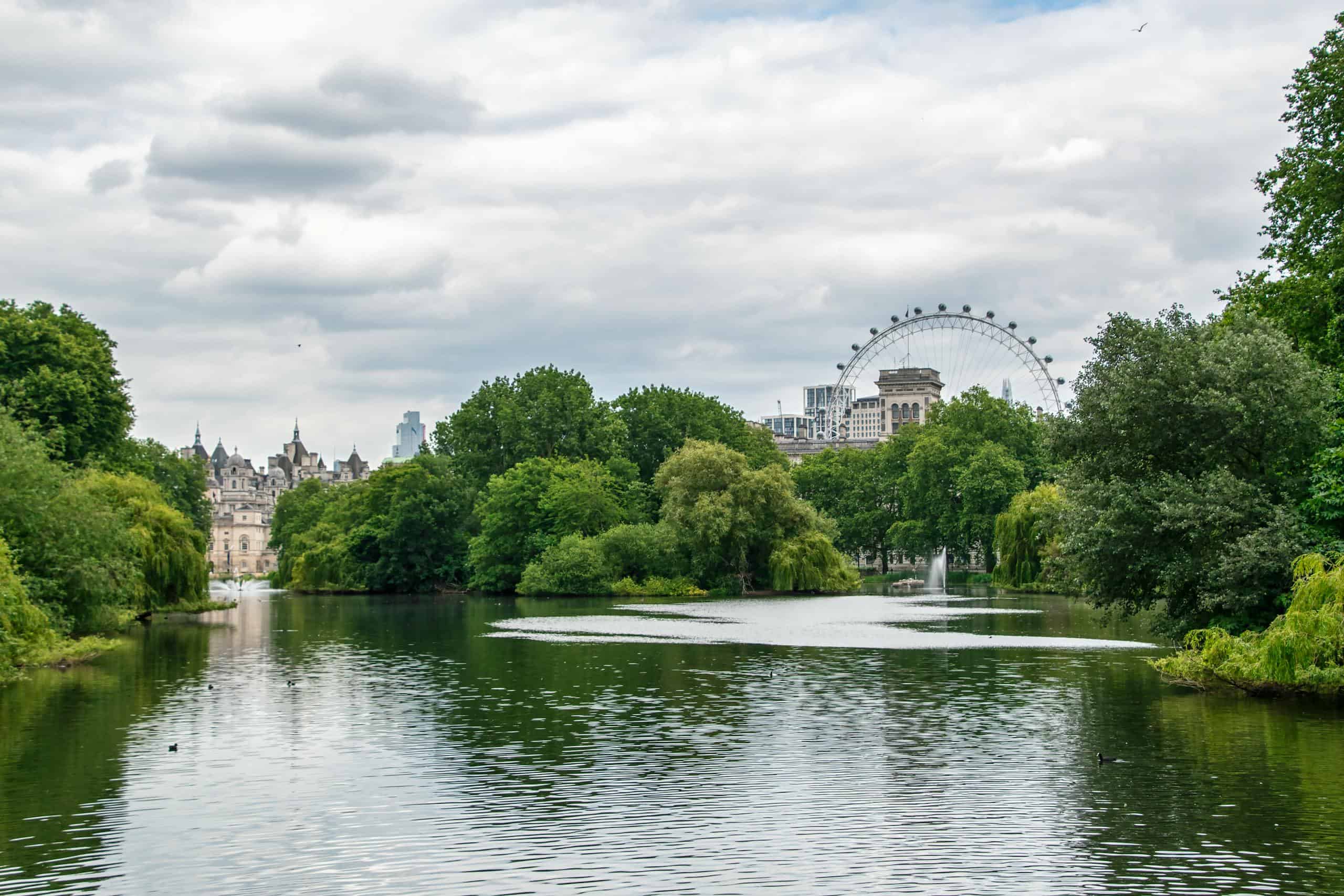 A picturesque view of the London Eye with lush greenery and a serene lake in St James's Park.