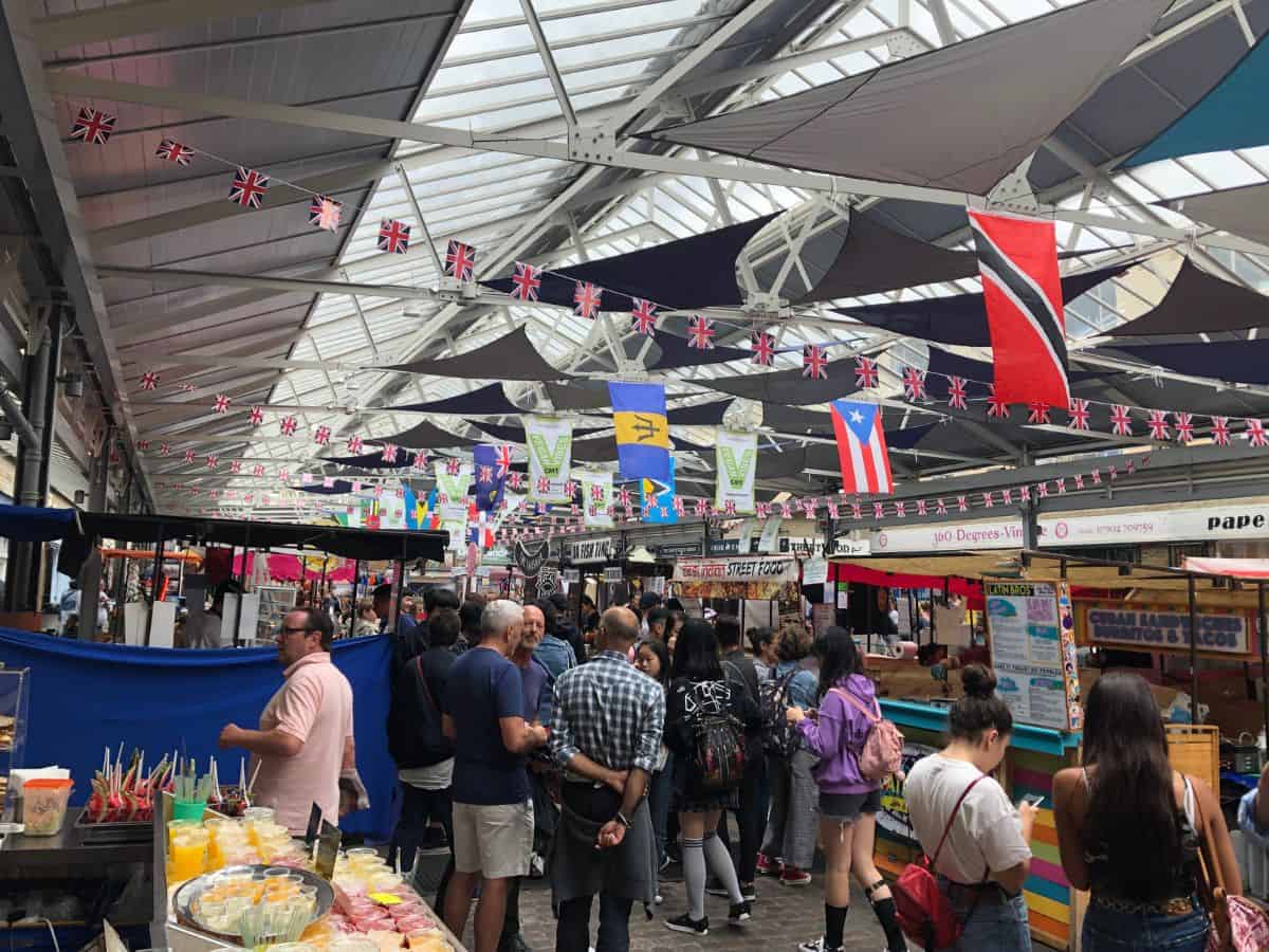Bustling lunchtime scene at Greenwich Market, London with food stalls and crowds of people moving through.