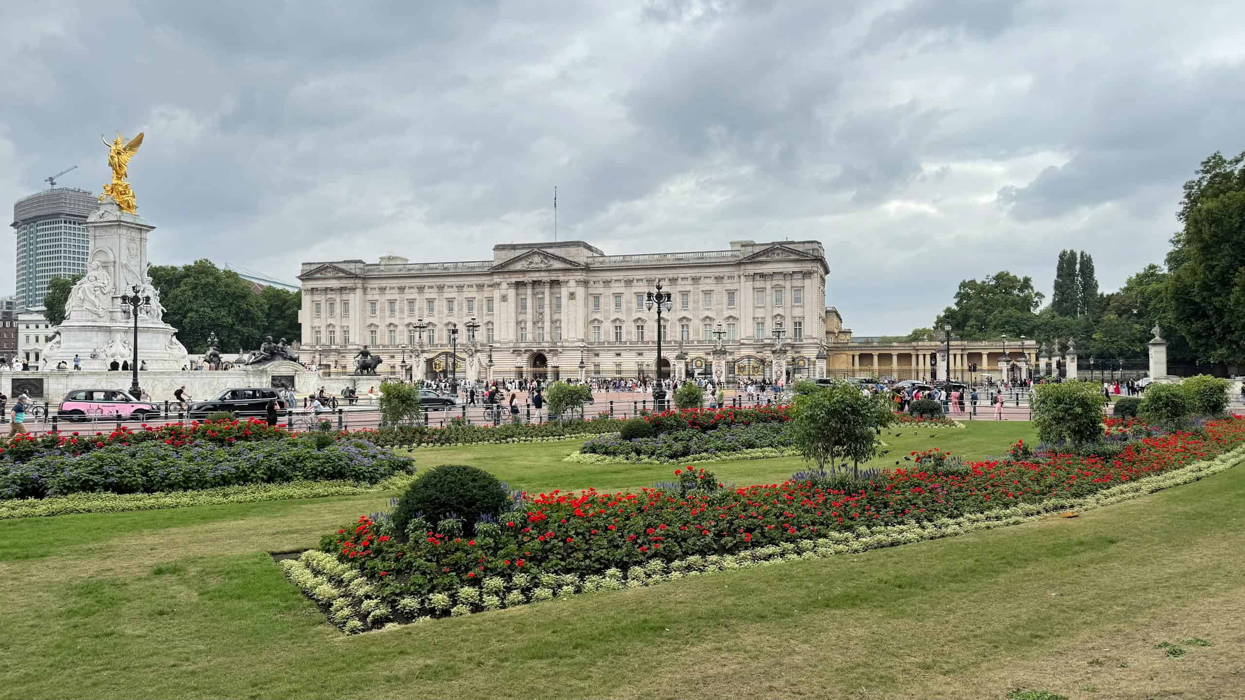 Iconic view of Buckingham Palace and Victoria Memorial in London, with lush gardens and cloudy skies.