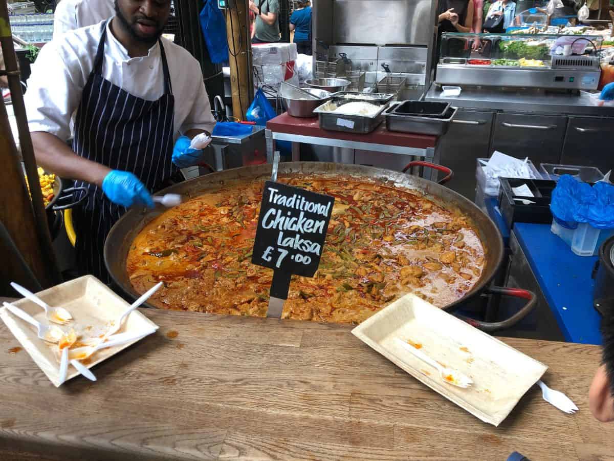 Food vendor serving a large dish of traditional chicken laksa at Borough Market in London