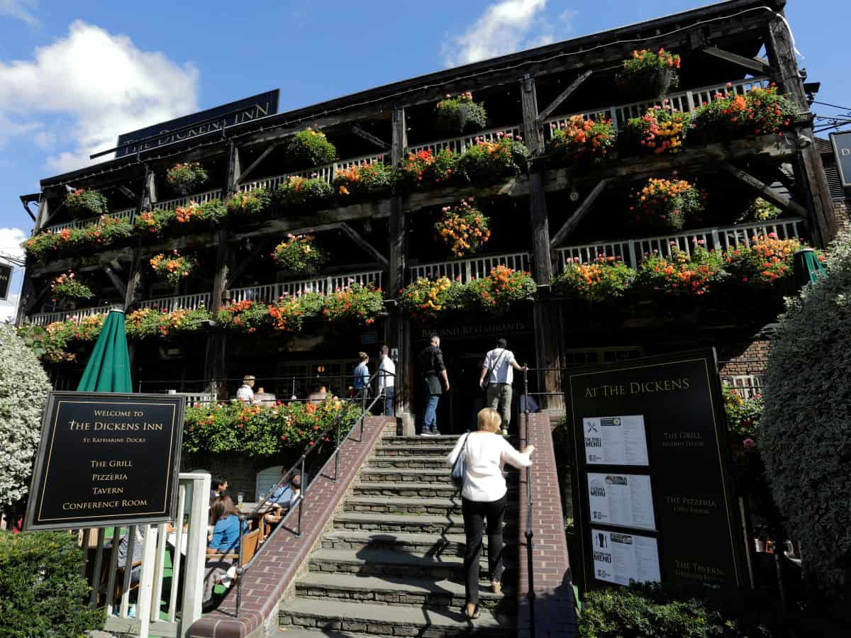 Historic wooden galleries of The Dickens Inn with colorful summer hanging baskets under a bright blue sky at St Katharine Docks in London