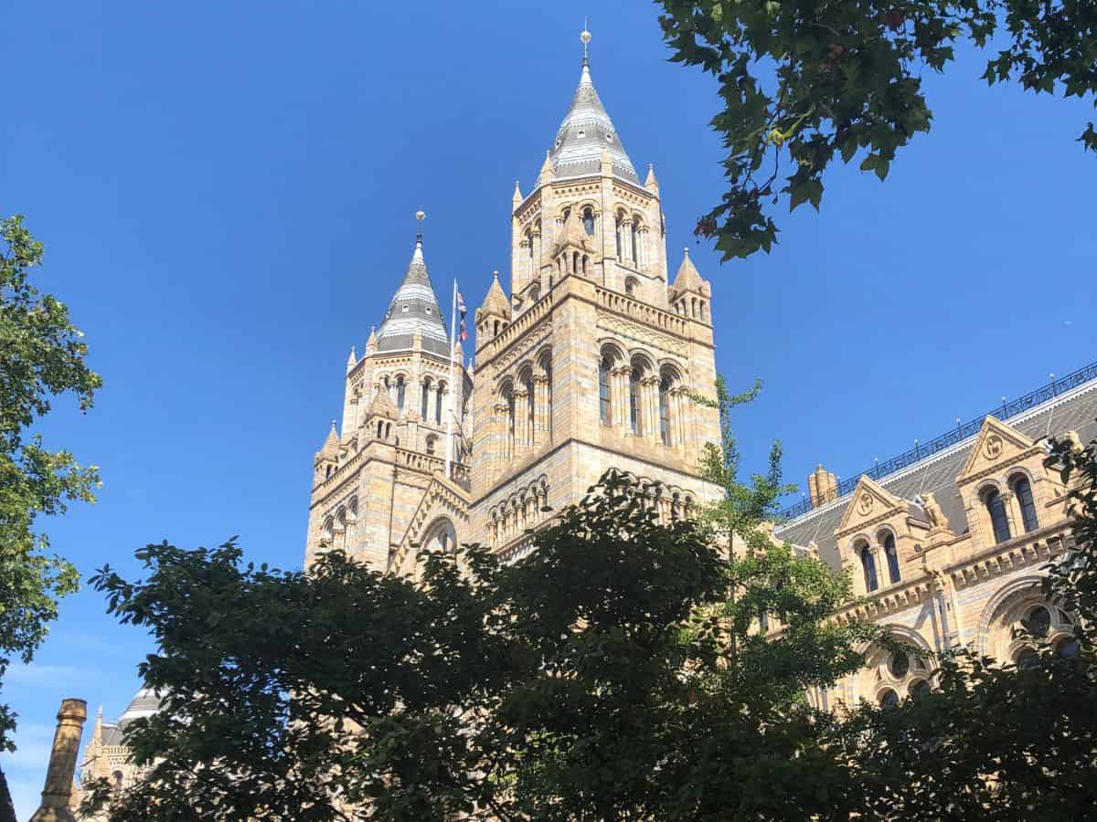 Romanesque architecture displayed on the towers at the Natural History Museum in South Kensington in London. as seen through trees on a sunny day.