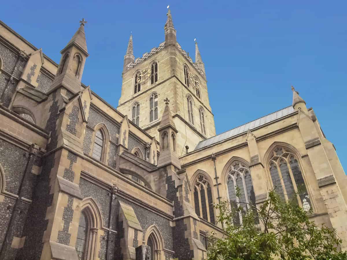 Gothic architecture of Southwark Cathedral in London looking up from street level against the backdrop of a blue sky.