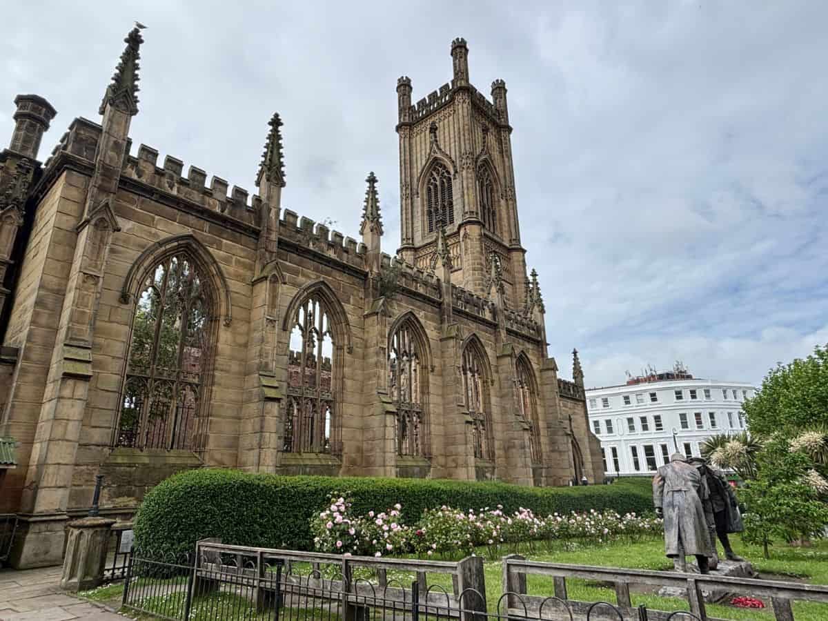 Liverpoo's bombed out church structure, also known as St. Lukes with gardens in front and iconic Christmas Truce Football Statue against a cloudy sky.