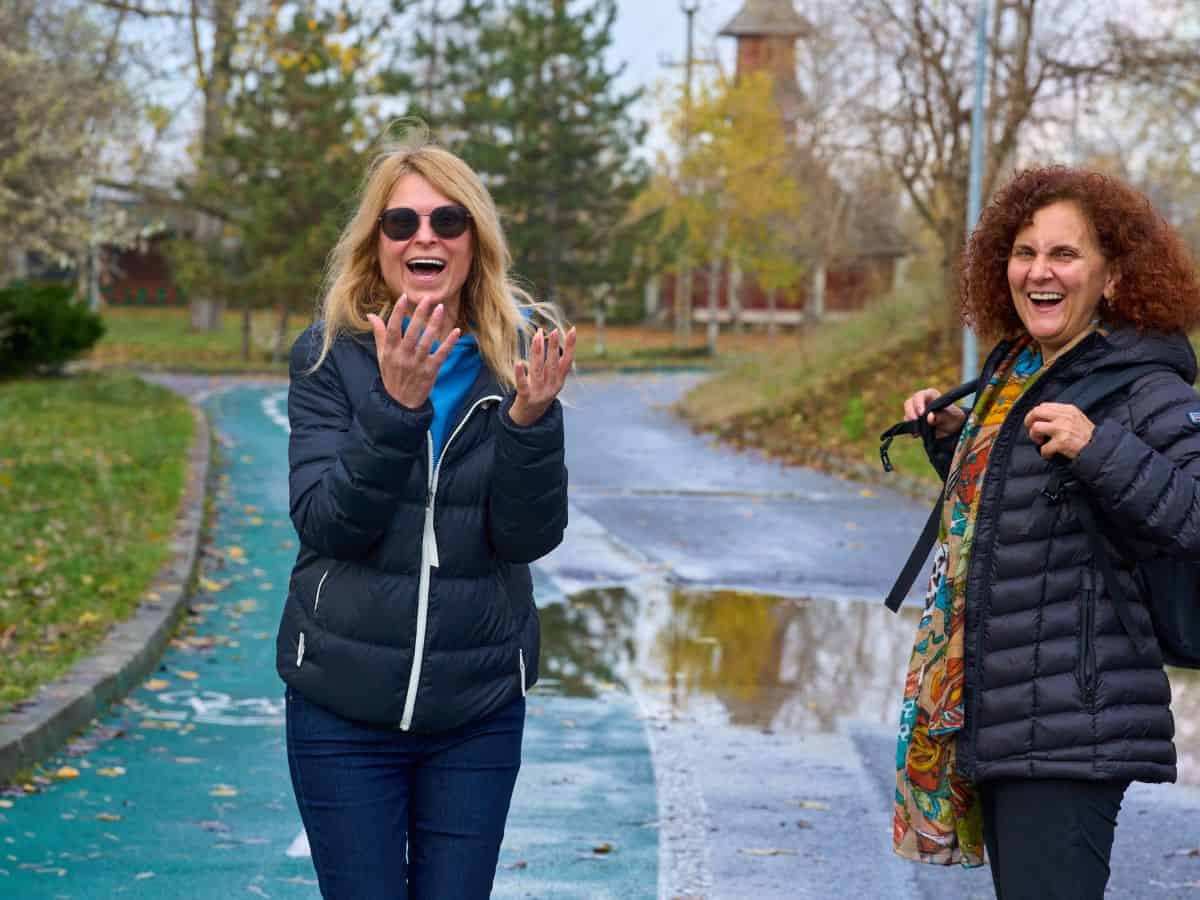 Two women in their 50s enjoying each others company and walking in a fall like area after rain. Both looking at the camera.