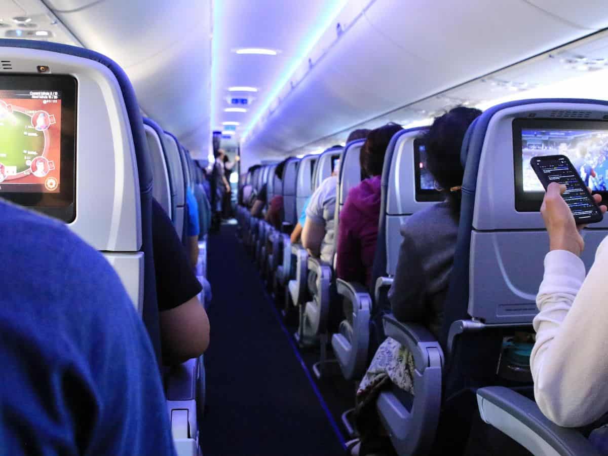 Interior of aircraft cabin with view of central aisle with passengers sitting on either side and interior lighting overhead