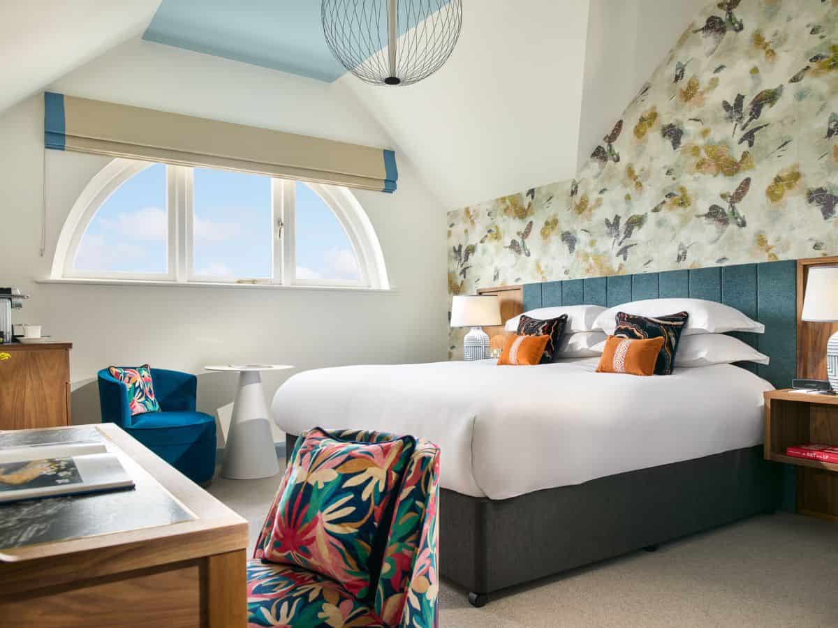 Interior view of a Deluxe King Room at Dublin's Dylan Hotel with colorful, bright wallpaper accent behind bed and semi circle arch window.
