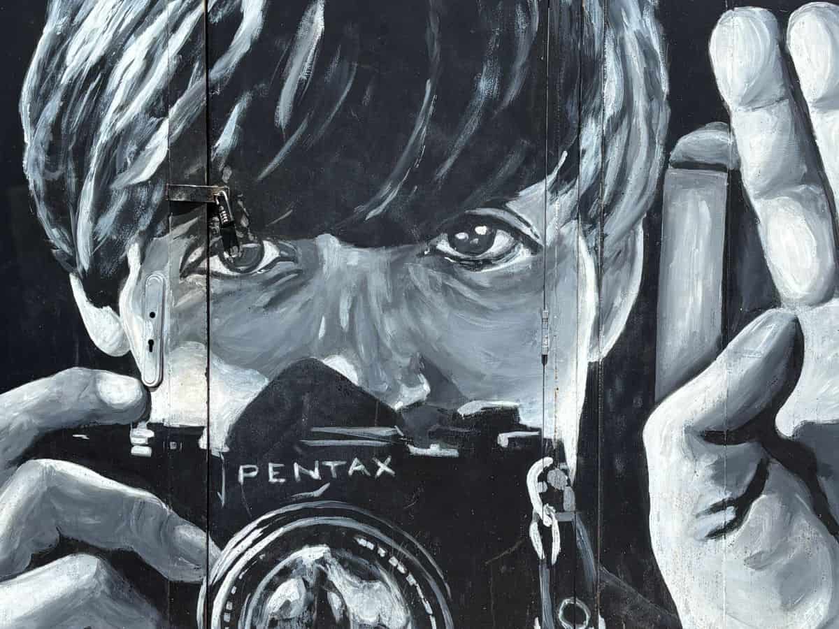 Black & white mural of Sir Paul McCartney's face and holding a camera and raising his right hand.