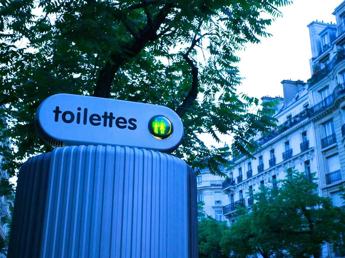 Parisian public toilet with sign on a leafy street in Paris.