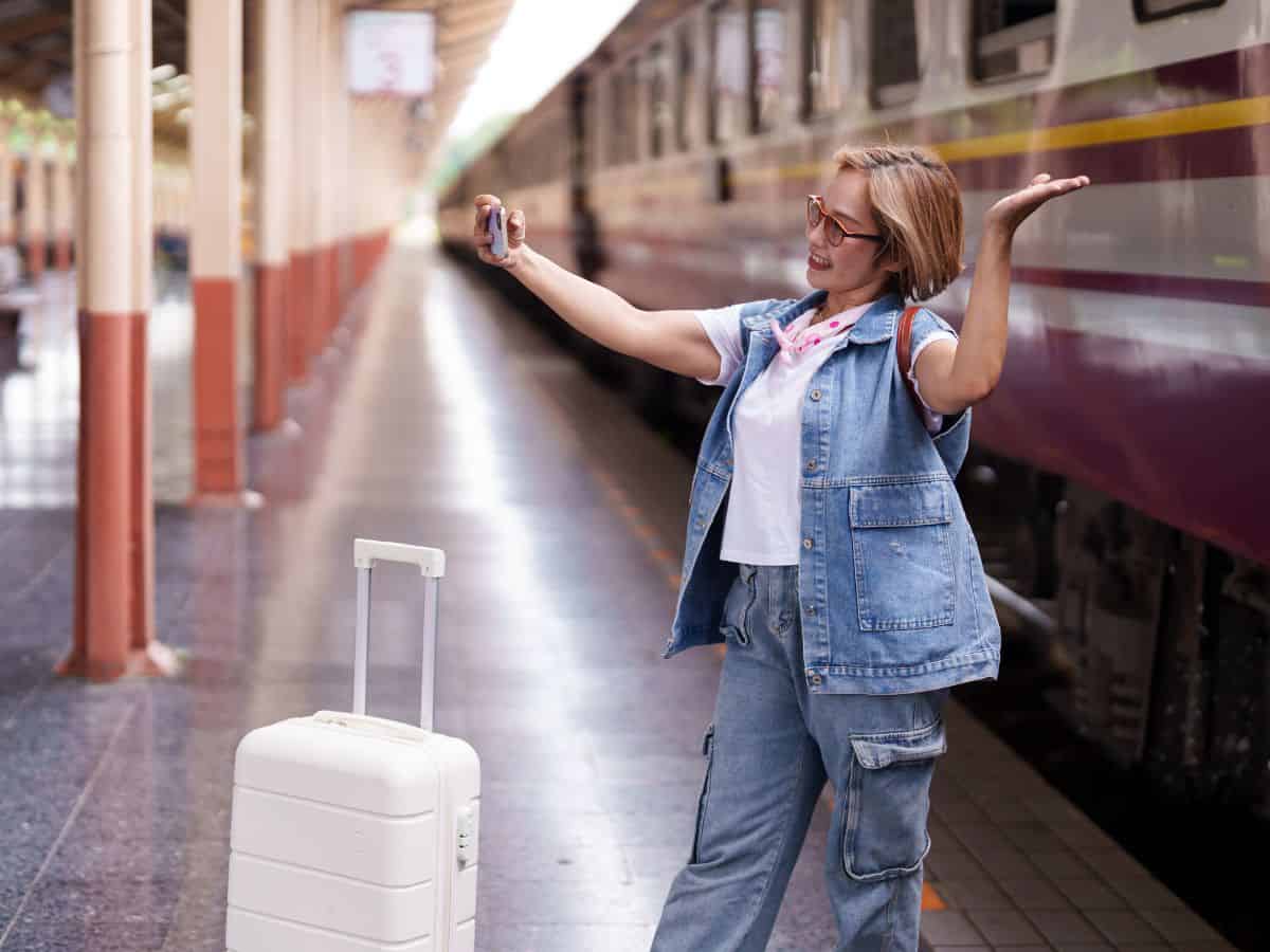 Solo female traveler standing on a train platform taking a selfie with her luggage in front.