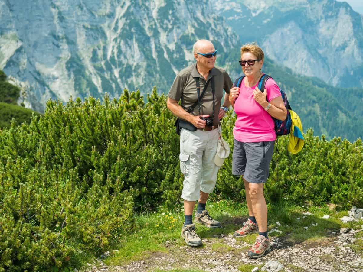 Couple in their late 60's dressed in hiking gear for summer against a mountain backdrop.
